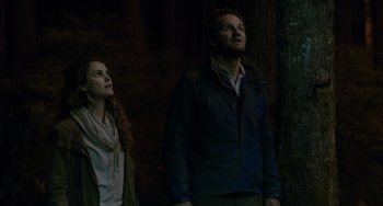 Movie still from “Dawn of the Planet of the Apes” (2014), directed by Matt Reeves – A man and a woman standing next to each other in front of a tree; Medium shot, Low angle