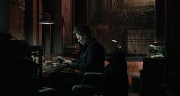 Movie still from “Dawn of the Planet of the Apes” (2014), directed by Matt Reeves – A man sitting at a table in front of a book; Medium shot, High angle