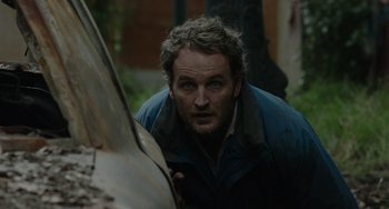 Movie still from “Dawn of the Planet of the Apes” (2014), directed by Matt Reeves – A man looking at the camera while standing next to a tree trunk; Close Up shot, Low angle