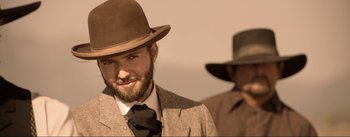 Movie still from “Dead for a Dollar” (2022), directed by Walter Hill – A man with a beard wearing a suit and a hat; Close Up shot, Over the shoulder angle