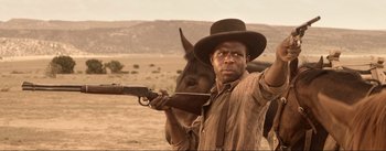 Movie still from “Dead for a Dollar” (2022), directed by Walter Hill – A man holding a gun and a horse in a field; Medium shot, Over the shoulder angle