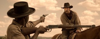 Movie still from “Dead for a Dollar” (2022), directed by Walter Hill – A man on a horse holding a gun and another man on a horse holding a gun; Medium shot, Over the shoulder angle