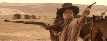 Movie still from “Dead for a Dollar” (2022), directed by Walter Hill – A man holding a gun and a horse in a field; Medium shot, Over the shoulder angle