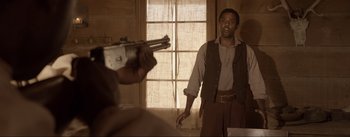 Movie still from “Dead for a Dollar” (2022), directed by Walter Hill – A man holding a gun in front of a window; Medium shot, Over the shoulder angle