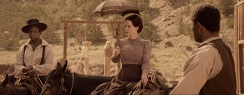 Movie still from “Dead for a Dollar” (2022), directed by Walter Hill – A woman sitting on top of a horse holding an umbrella; Medium shot, Over the shoulder angle