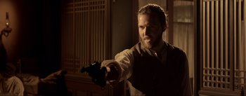 Movie still from “Dead for a Dollar” (2022), directed by Walter Hill – A man holding a gun and pointing to the ground; Medium shot, Over the shoulder angle