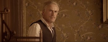 Movie still from “Dead for a Dollar” (2022), directed by Walter Hill – A man in a vest standing in front of a floral wallpaper; Close Up shot, Over the shoulder angle