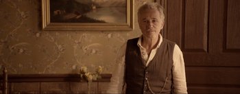 Movie still from “Dead for a Dollar” (2022), directed by Walter Hill – An older man standing in front of a painting in a living room; Medium shot, Over the shoulder angle