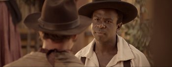 Movie still from “Dead for a Dollar” (2022), directed by Walter Hill – A man wearing a brown hat and a white shirt looking at another man; Close Up shot, Over the shoulder angle