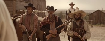 Movie still from “Dead for a Dollar” (2022), directed by Walter Hill – A man holding a rifle while standing next to a horse; Medium shot, Low angle