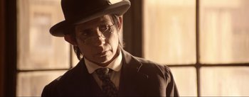 Movie still from “Dead for a Dollar” (2022), directed by Walter Hill – A man in a suit and tie wearing glasses and a hat; Close Up shot, Over the shoulder angle