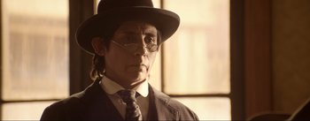 Movie still from “Dead for a Dollar” (2022), directed by Walter Hill – A man in a hat and glasses wearing a suit and tie; Close Up shot, Low angle