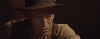 Movie still from “Dead for a Dollar” (2022), directed by Walter Hill – An older man wearing a hat with a pipe in his mouth; Close Up shot, Over the shoulder angle