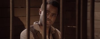 Movie still from “Dead for a Dollar” (2022), directed by Walter Hill – A man in a brown jacket behind bars; Close Up shot, Over the shoulder angle