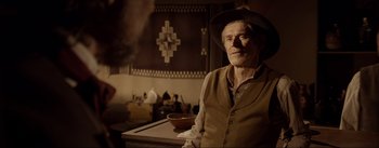 Movie still from “Dead for a Dollar” (2022), directed by Walter Hill – An old man wearing a hat sitting at a table in front of a bowl; Medium shot, Over the shoulder angle