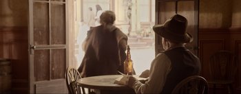Movie still from “Dead for a Dollar” (2022), directed by Walter Hill – A man sitting at a table with a bottle of whiskey; Medium shot, Over the shoulder angle