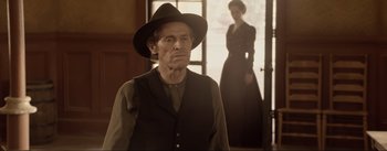 Movie still from “Dead for a Dollar” (2022), directed by Walter Hill – An old man wearing a black hat and a woman wearing a black dress; Medium shot, Over the shoulder angle