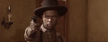 Movie still from “Dead for a Dollar” (2022), directed by Walter Hill – A man in a hat and a tie holding a gun; Close Up shot, Low angle