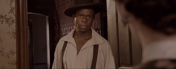 Movie still from “Dead for a Dollar” (2022), directed by Walter Hill – A man wearing a hat and suspenders standing in front of a wall; Close Up shot, Over the shoulder angle