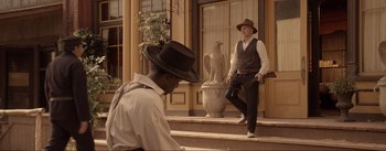 Movie still from “Dead for a Dollar” (2022), directed by Walter Hill – A man in a hat sitting on steps next to another man in a hat; Wide shot, Over the shoulder angle