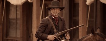 Movie still from “Dead for a Dollar” (2022), directed by Walter Hill – A man holding a gun while standing next to a building; Medium shot, Over the shoulder angle