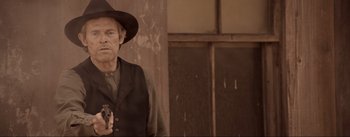 Movie still from “Dead for a Dollar” (2022), directed by Walter Hill – A man in a hat and a vest holding a gun; Medium shot, Over the shoulder angle