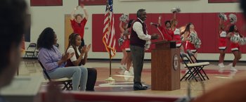 Movie still from “Dear Evan Hansen” (2021), directed by Stephen Chbosky – A man standing at a podium in front of an american flag; Wide shot, Over the shoulder angle