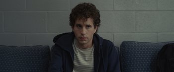 Movie still from “Dear Evan Hansen” (2021), directed by Stephen Chbosky – A man with curly brown hair sitting in front of a brick wall; Close Up shot, Over the shoulder angle
