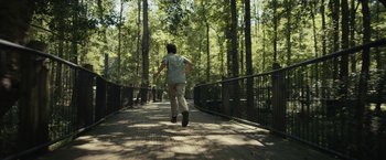 Movie still from “Dear Evan Hansen” (2021), directed by Stephen Chbosky – A man walking across a bridge in the woods; Wide shot, High angle