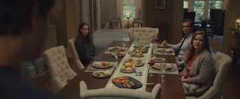 Movie still from “Dear Evan Hansen” (2021), directed by Stephen Chbosky – A woman sitting at a dinner table with plates of food on it; Wide shot, Over the shoulder angle