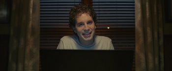 Movie still from “Dear Evan Hansen” (2021), directed by Stephen Chbosky – A man sitting in front of a computer smiling; Close Up shot, Over the shoulder angle