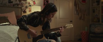 Movie still from “Dear Evan Hansen” (2021), directed by Stephen Chbosky – A woman is playing an electric guitar in a room; Medium shot, Over the shoulder angle