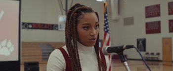 Movie still from “Dear Evan Hansen” (2021), directed by Stephen Chbosky – A woman with long braids standing in front of a microphone in front of an american flag; Close Up shot, Over the shoulder angle