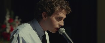 Movie still from “Dear Evan Hansen” (2021), directed by Stephen Chbosky – A man with curly brown hair is holding a microphone; Close Up shot, Low angle