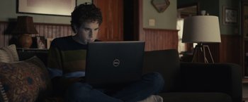 Movie still from “Dear Evan Hansen” (2021), directed by Stephen Chbosky – A man sitting on a couch looking at a laptop computer; Medium shot, High angle
