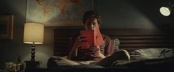 Movie still from “Dear Evan Hansen” (2021), directed by Stephen Chbosky – A man sitting in a bed reading a book; Medium shot, High angle