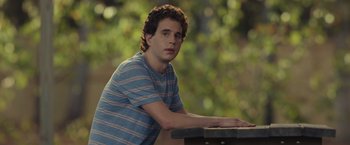 Movie still from “Dear Evan Hansen” (2021), directed by Stephen Chbosky – A young man sitting on a bench in a park; Close Up shot, Over the shoulder angle