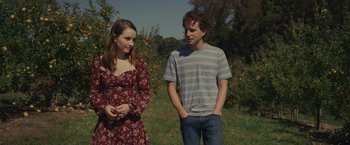 Movie still from “Dear Evan Hansen” (2021), directed by Stephen Chbosky – A young man and a young woman standing next to each other in an apple orchard; Medium shot, Over the shoulder angle