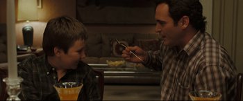 Movie still from “Two Lovers” (2008), directed by James Gray – A man and a boy are eating food together; Medium shot, Over the shoulder angle
