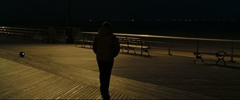 Movie still from “Two Lovers” (2008), directed by James Gray – A person is walking on a boardwalk at night; Wide shot, Over the shoulder angle