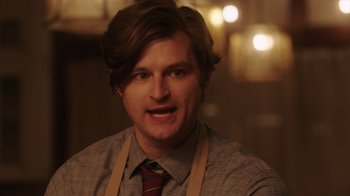 Movie still from “Deborah” (2022), directed by Noga Pnueli – A man wearing an apron and wearing a tie; Close Up shot, Over the shoulder angle