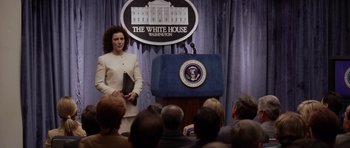 Movie still from “Deep Impact” (1998), directed by Mimi Leder – A woman standing at a podium in front of a group of people; Medium shot, Over the shoulder angle