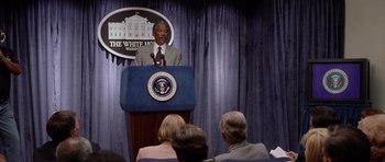 Movie still from “Deep Impact” (1998), directed by Mimi Leder – A man standing at a podium in front of an audience; Medium shot, Low angle