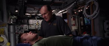 Movie still from “Deep Impact” (1998), directed by Mimi Leder – A man standing next to a man laying on a bed; Medium shot, Over the shoulder angle