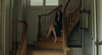 Movie still from “Deep Water” (2022), directed by Adrian Lyne – A woman sitting on the bottom step of a wooden staircase; Wide shot, High angle