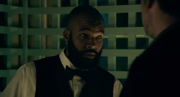 Movie still from “Deep Water” (2022), directed by Adrian Lyne – A man with a beard wearing a vest and a bow tie; Close Up shot, Over the shoulder angle