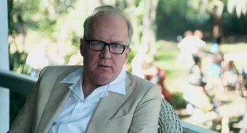 Movie still from “Deep Water” (2022), directed by Adrian Lyne – An older man wearing glasses and a tan jacket; Close Up shot, Over the shoulder angle