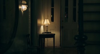Movie still from “Deep Water” (2022), directed by Adrian Lyne – A table with a lamp in the middle of a room; Wide shot, Over the shoulder angle