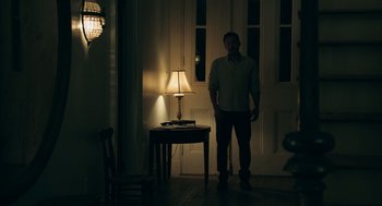 Movie still from “Deep Water” (2022), directed by Adrian Lyne – A man standing in front of a lamp in a room; Wide shot, Low angle