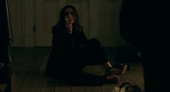 Movie still from “Deep Water” (2022), directed by Adrian Lyne – A woman sitting on the ground smoking a cigarette; Medium shot, High angle